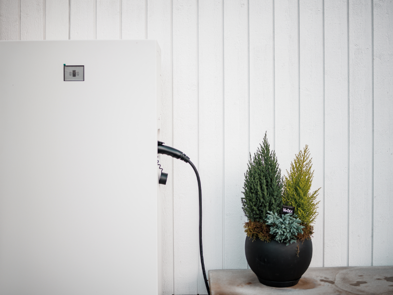 Detaljbild av Emaldo Power Core hembatteri – installerat i bostad i Solna Närbild på Emaldo hembatteri i Solna – anslutet och installerat intill yttervägg med dekorativa växter.